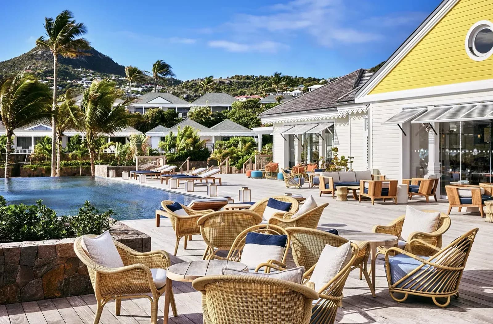 Rosewood Le Guanahani – Poolterrasse mit Korbmöbeln vor dem gelben Hauptgebäude